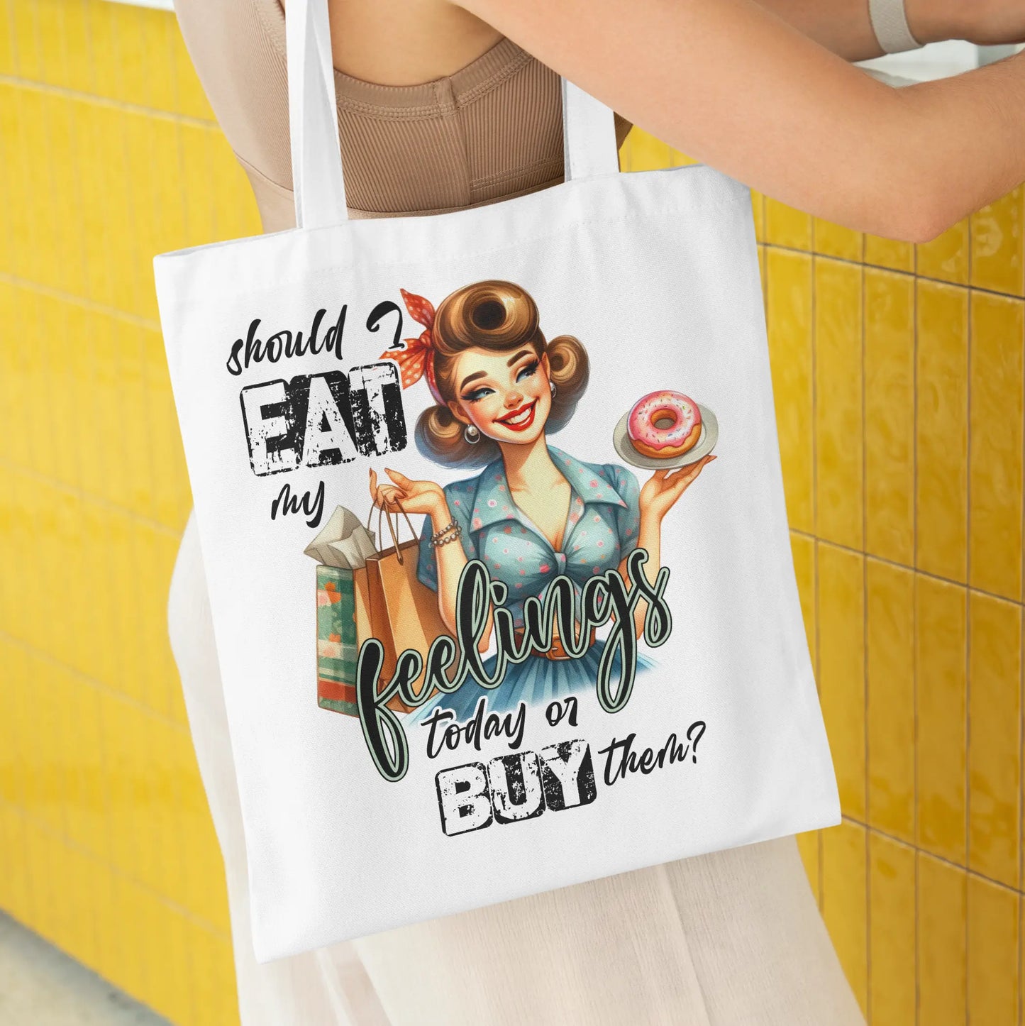 White tote bag with a retro pin-up girl holding a donut and shopping bags, with the quote:
“Should I eat my feelings today or buy them?”