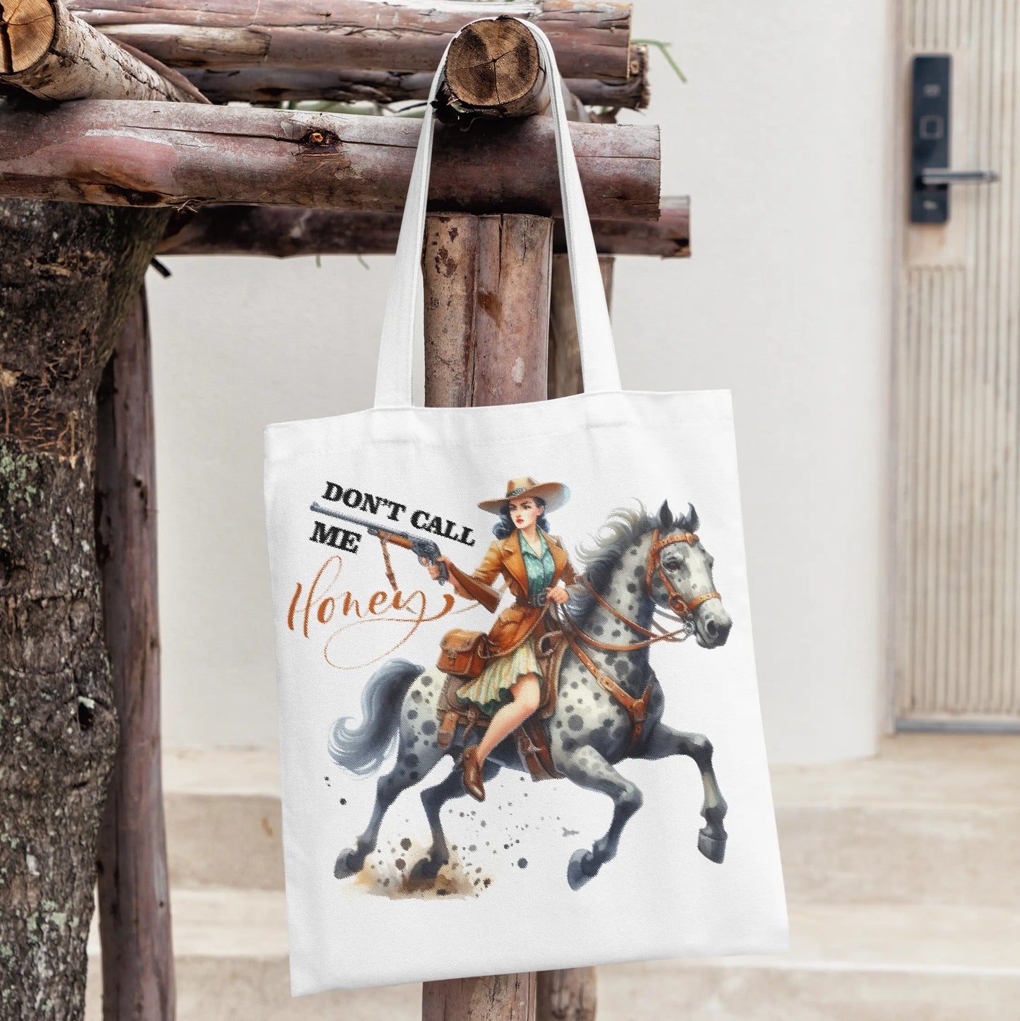 White tote bag with a fierce cowgirl on a horse, holding a gun, and bold text: “Don’t Call Me Honey.”