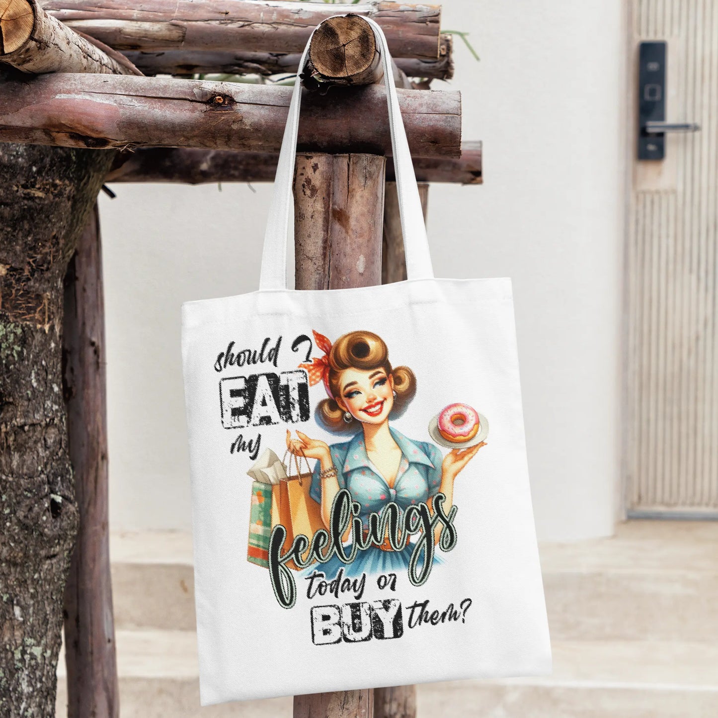 White tote bag with a retro pin-up girl holding a donut and shopping bags, with the quote:
“Should I eat my feelings today or buy them?”