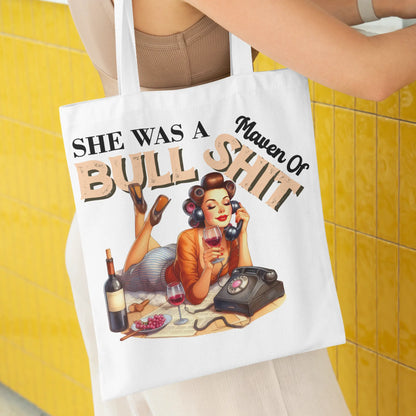 White tote bag featuring a glamorous retro woman with a wine glass and rotary phone.
Text reads: "She Was a Maven of Bullshit"