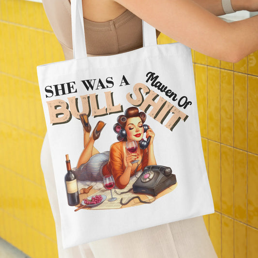 White tote bag featuring a glamorous retro woman with a wine glass and rotary phone.
Text reads: "She Was a Maven of Bullshit"